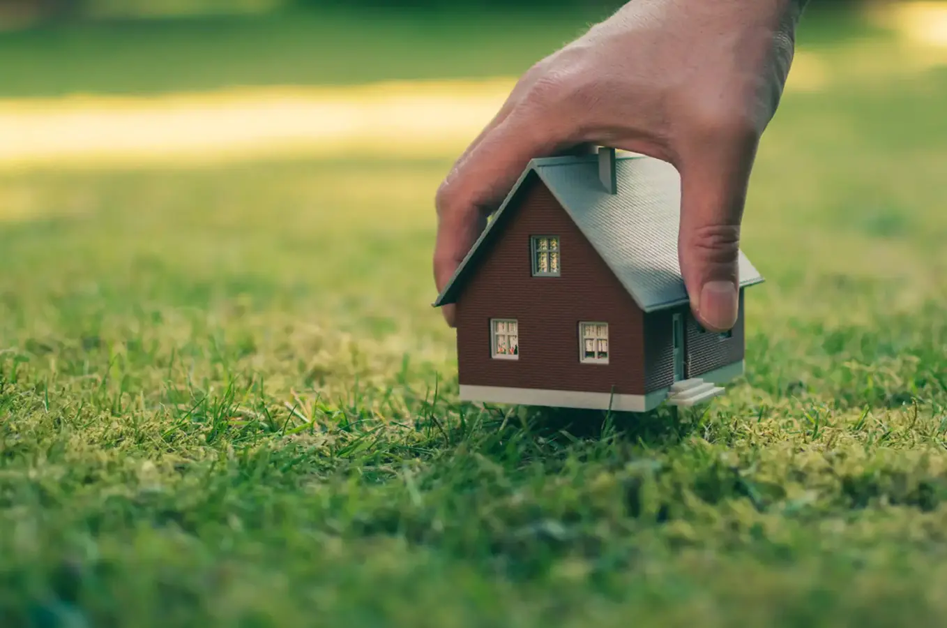 Hand placing small house on grass